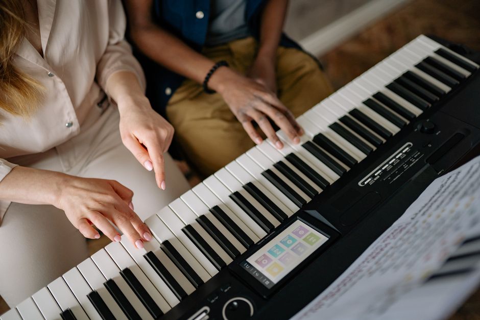 Close-up of two pairs of hands learning to play on a piano keyboard during a music lesson.