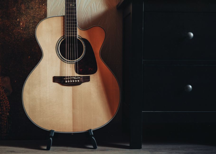A beautifully crafted acoustic guitar placed neatly beside a dark wooden cabinet in a dimly lit room.