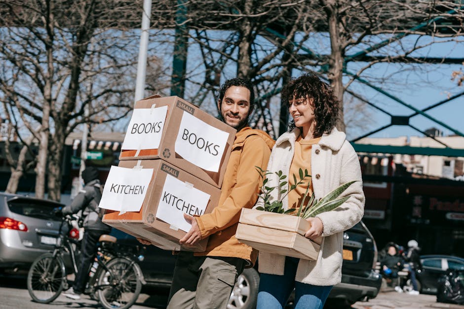 A joyful couple carrying boxes labeled books and kitchen in an urban setting, symbolizing a fresh start.