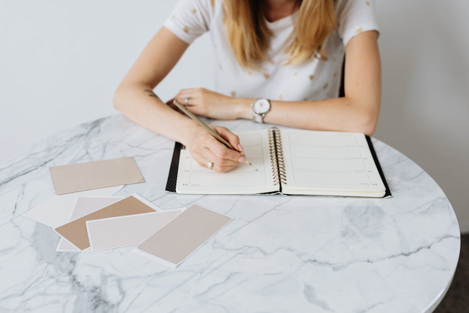 Woman writing interior design plans on notebook at a marble table.