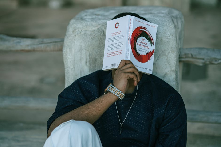 A man reads 'The Courage to Be Disliked' in an outdoor setting, focusing on self-improvement and mindfulness.