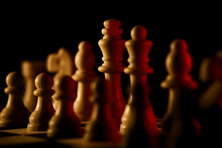 Chess pieces lit dramatically on a black background, evoking strategy and focus.