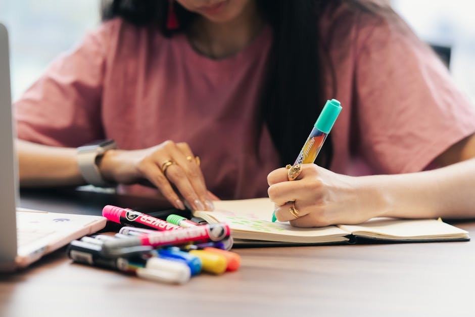 Focused young woman writing with vibrant markers in a notebook, creating ideas.