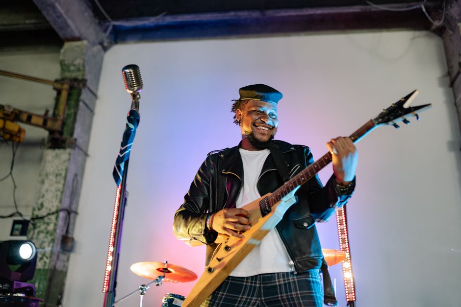 Talented guitarist in a leather jacket playing music passionately on stage with vibrant lighting.