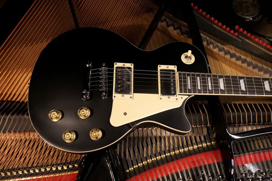 A black electric guitar resting on the strings of a grand piano, showcasing musical harmony.