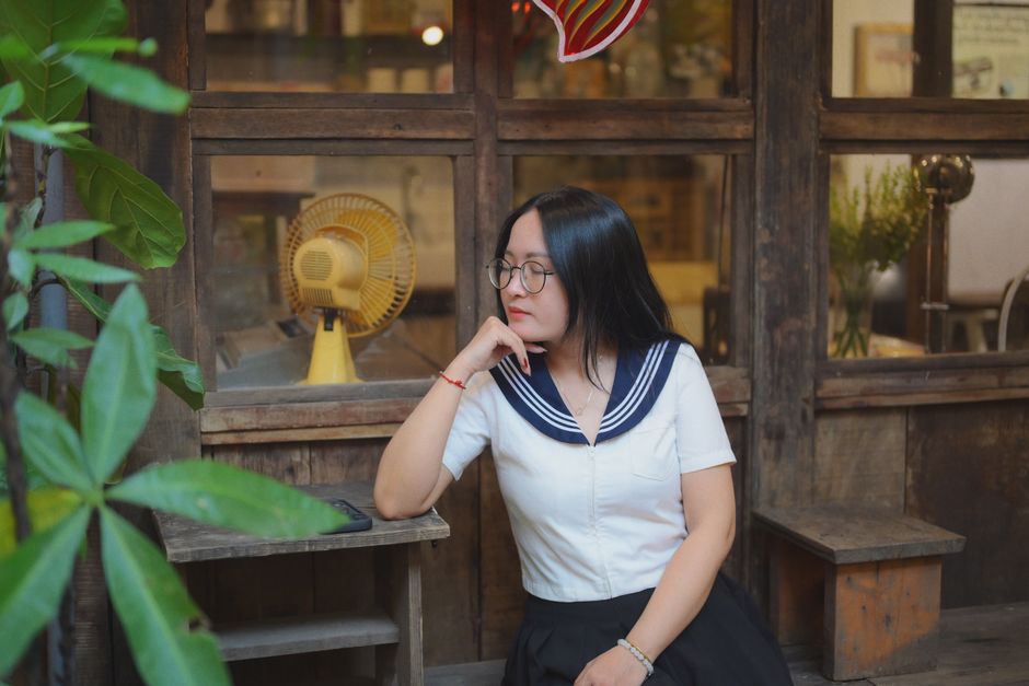 A woman in stylish attire sits thoughtfully in a rustic setting with vintage decor.
