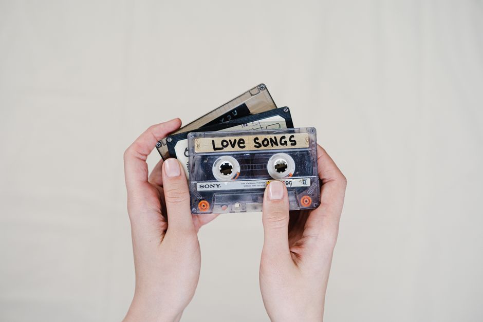 Hands holding cassette tapes labeled 'Love Songs', highlighting 90s nostalgia.
