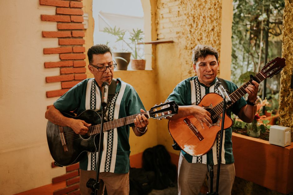 Two male musicians playing guitars and singing indoors in a vibrant, rustic setting.