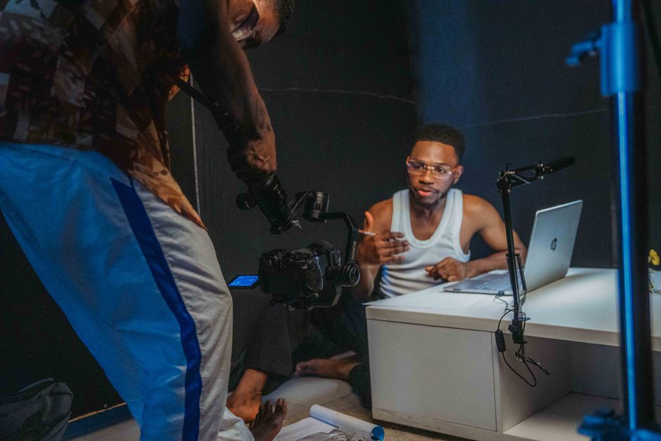 Young black men filming a casual video with laptop and camera in a home studio setting.