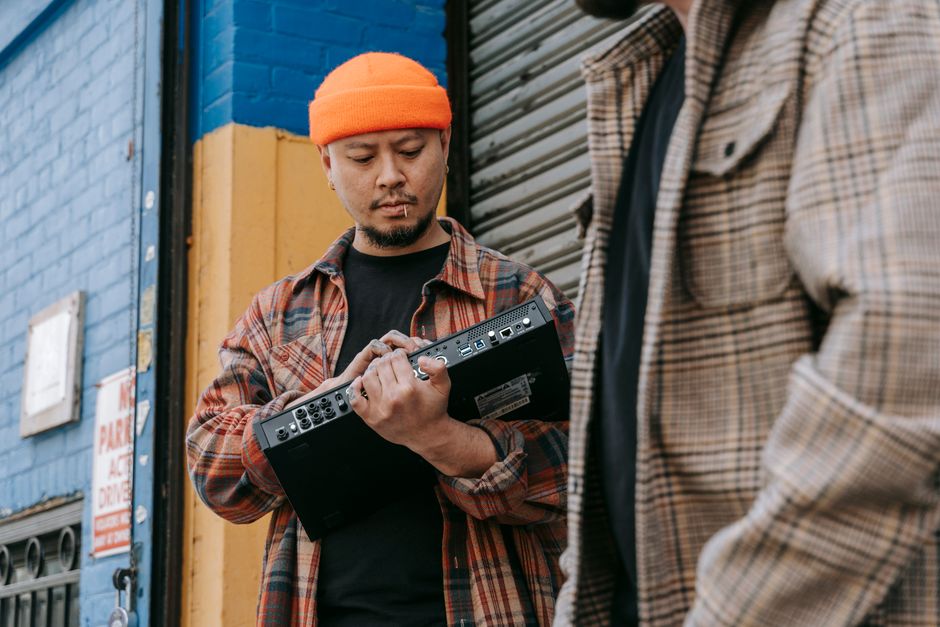 Musician holding audio equipment next to a colorful wall in a city street.
