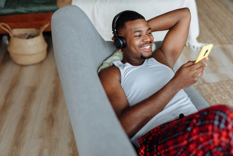 A happy man in casual wear listens to music on the couch enjoying his leisure time.