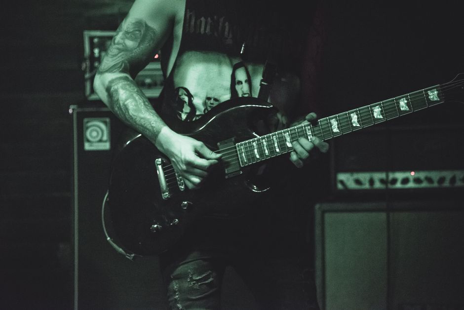 Musician with tattoos playing an electric guitar on stage in a dark, moody setting.