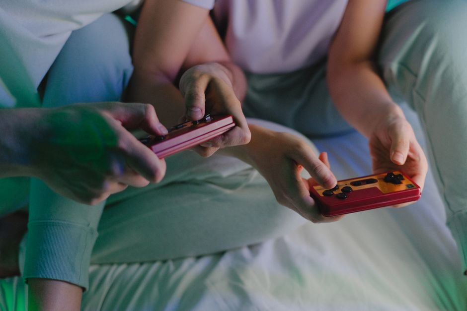 Close-up of a couple's hands holding retro game controllers while gaming indoors.