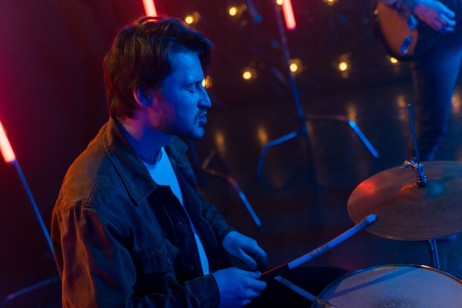 A man playing drums with colorful neon lights and bokeh background.