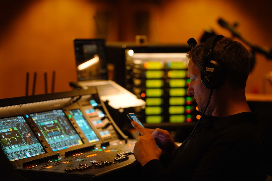 A sound engineer in a studio, focused on audio equipment and a smartphone.